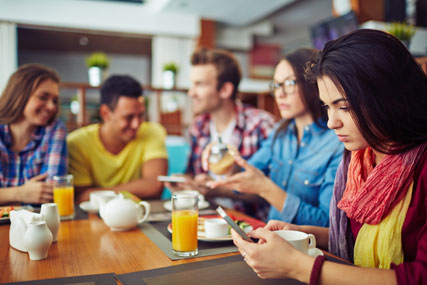 Woman checking notifications on phone while at breakfast with friends